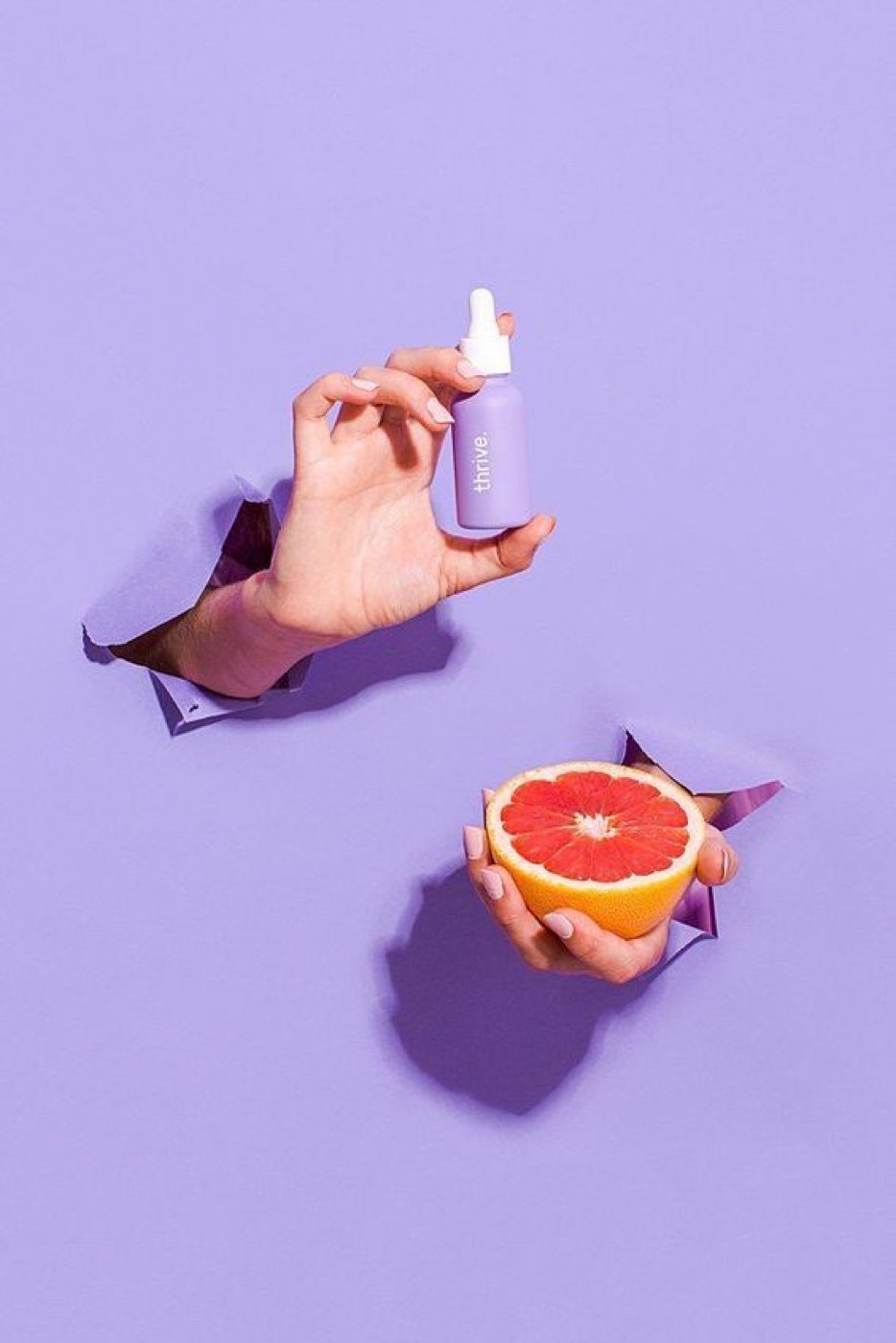 Branded serum bottle and grapefruit on a lilac backdrop